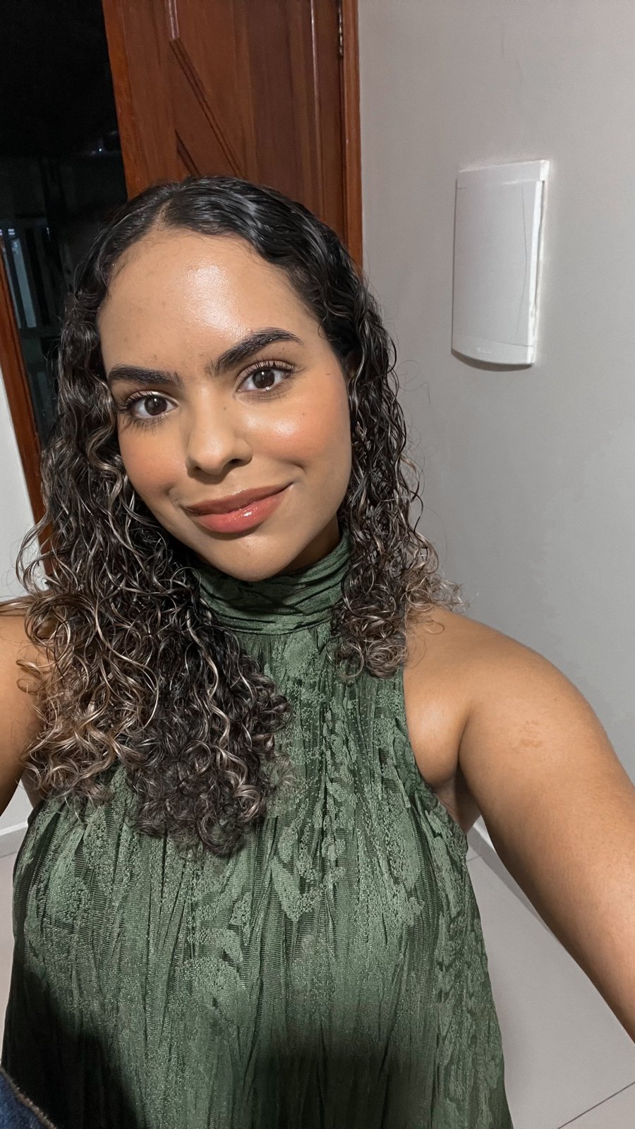 Foto de Raquel Rebouças sorrindo, com cabelo cacheado e blusa verde